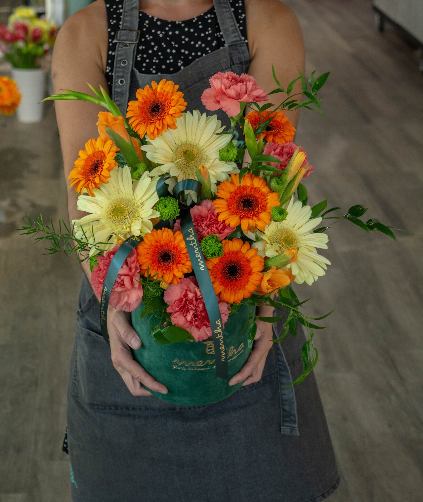 Cutie de catifea verde cu gerbera și garoafe într-o explozie de culori delicate.