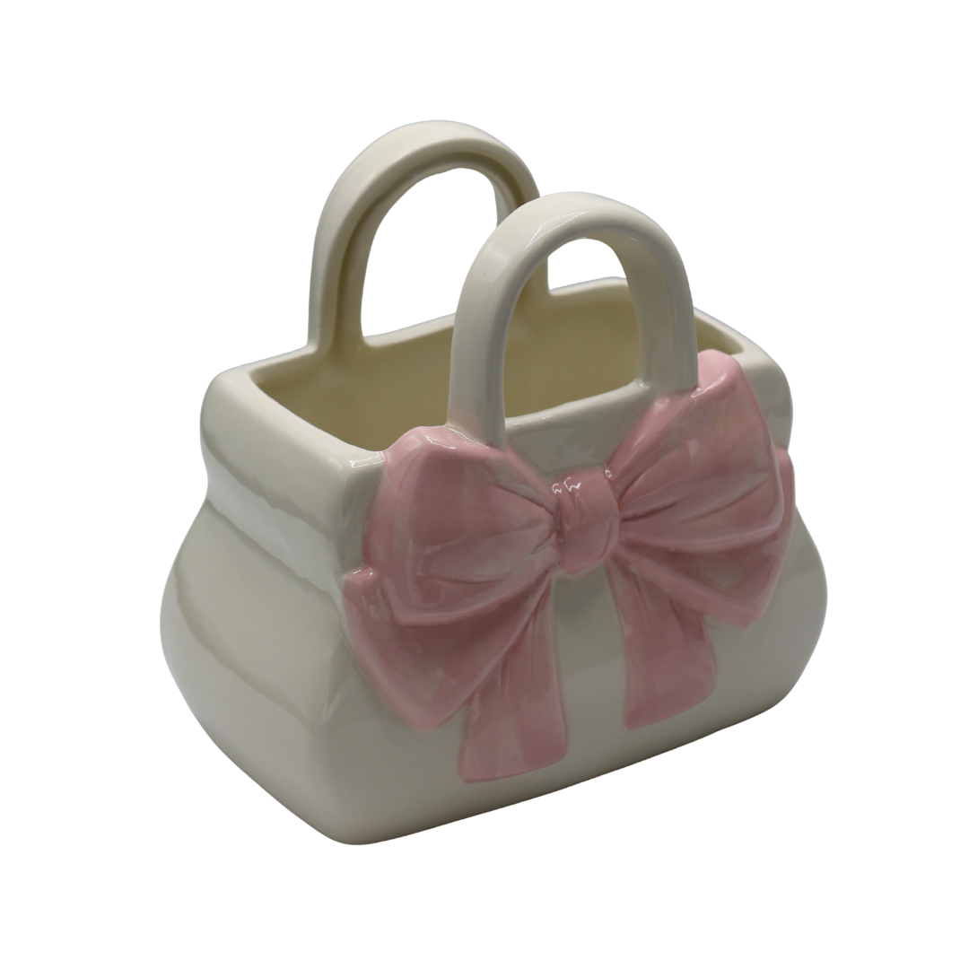 Vază decorativă din ceramică în formă de poșetă, cu finisaj alb și detalii roz tip fontă, creată pentru decoruri feminine și elegante. Designul modern inspirat din lumea fashion adaugă personalitate și rafinament oricărui spațiu interior și completează perfect dormitoarele, dressingurile, livingurile moderne sau birourile creative. Este ideală pentru flori decorative și poate fi oferită cadou la aniversări, casă nouă sau ocazii speciale pentru femei pasionate de accesorii decorative elegante.
