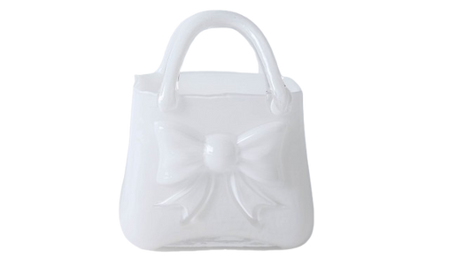 Vază decorativă din sticlă albă în formă de poșetă, concepută pentru interioare luminoase și elegante. Designul său curat adaugă rafinament și simplitate, fiind ideală pentru decor minimalist sau modern. Se potrivește perfect cu flori delicate și este o alegere excelentă pentru cadouri de casă nouă sau decoruri premium.